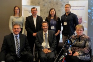 À l’avant, dans l’ordre habituel : le premier ministre Alward, qui est assis sur un fauteuil roulant multisport; Courtney Keenan, président de Capacité Nouveau-Brunswick; et la ministre des Collectivités saines et inclusives, Dorothy Shephard, assise sur un vélo à main. À l’arrière, dans l’ordre habituel : Meaghan Donahue, athlète et coordonnatrice des services d'entraînement, Centre canadien multisport atlantique; Darcy McKillop, directeur général, Sport Nouveau-Brunswick; Sandi Ware, coordonnatrice du service de prêt d’équipement, Para Nouveau-Brunswick; et Gregory Cutler, président du comité des loisirs inclusifs de Recreation New Brunswick.